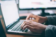 Mains tapant sur le clavier d'un ordinateur portable, second écran flou en arrière-plan