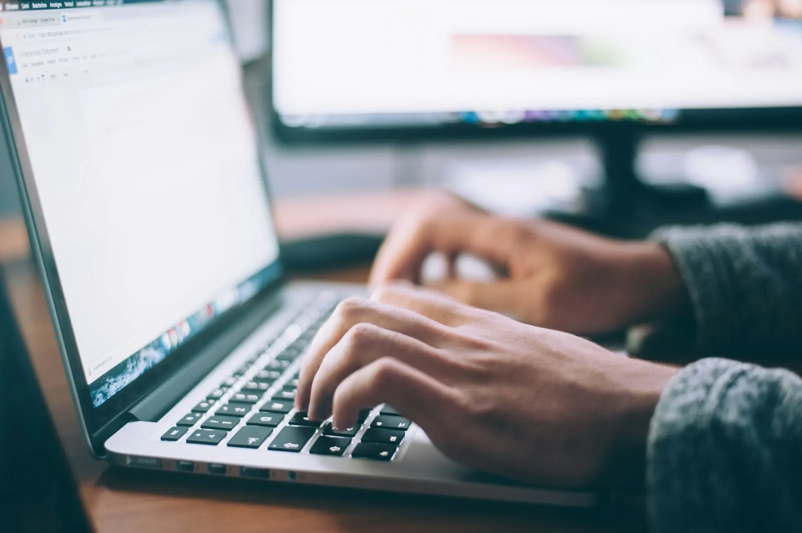 Mains tapant sur le clavier d'un ordinateur portable, second écran flou en arrière-plan