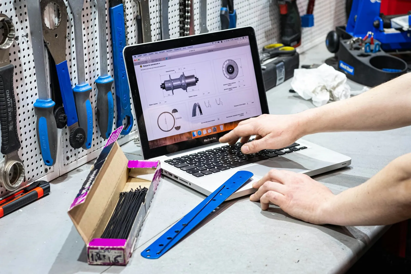 Mains sur le clavier d’un ordinateur portable posé sur l’établi d’un atelier, outils accrochés au mur