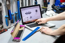 Mains sur le clavier d’un ordinateur portable posé sur l’établi d’un atelier, outils accrochés au mur